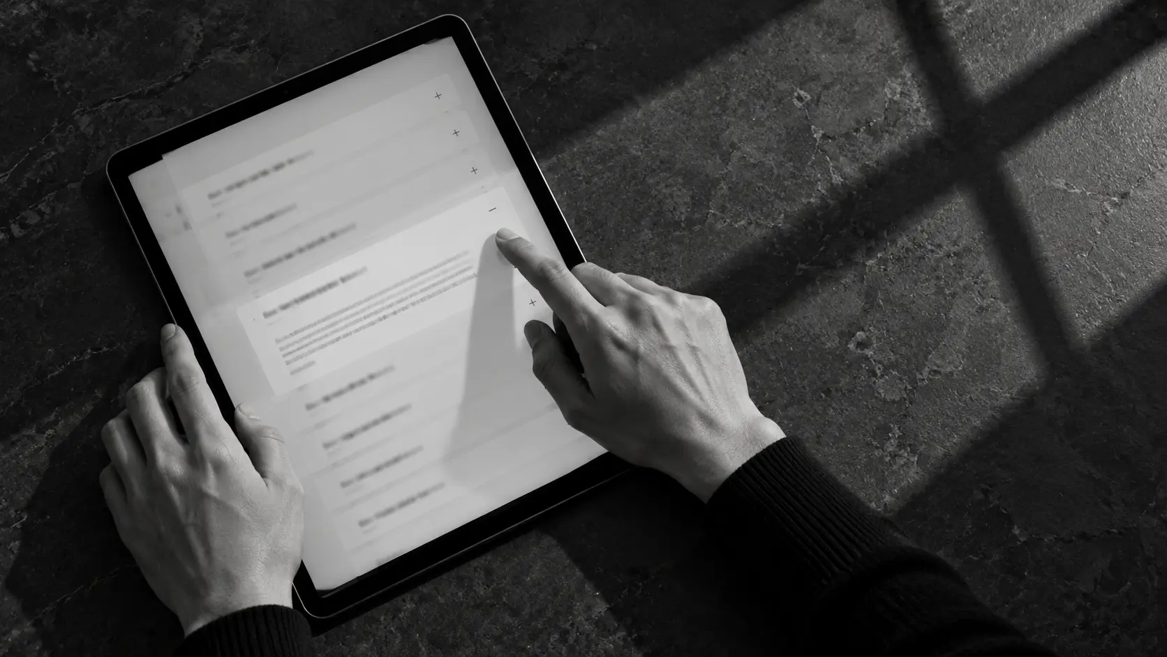 タブレットの質問一覧を指で開く手元を、真上から捉えた白黒画像。