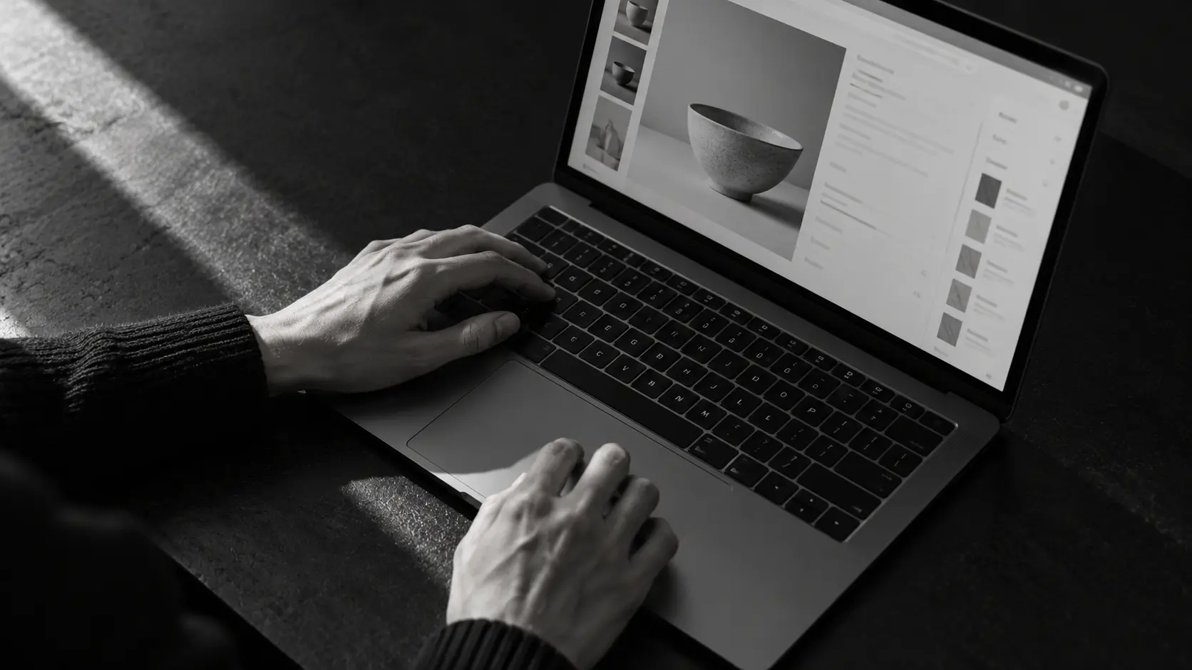 ノートパソコンの商品編集画面とキーボードを操作する手元を、斜め上から捉えた白黒画像。